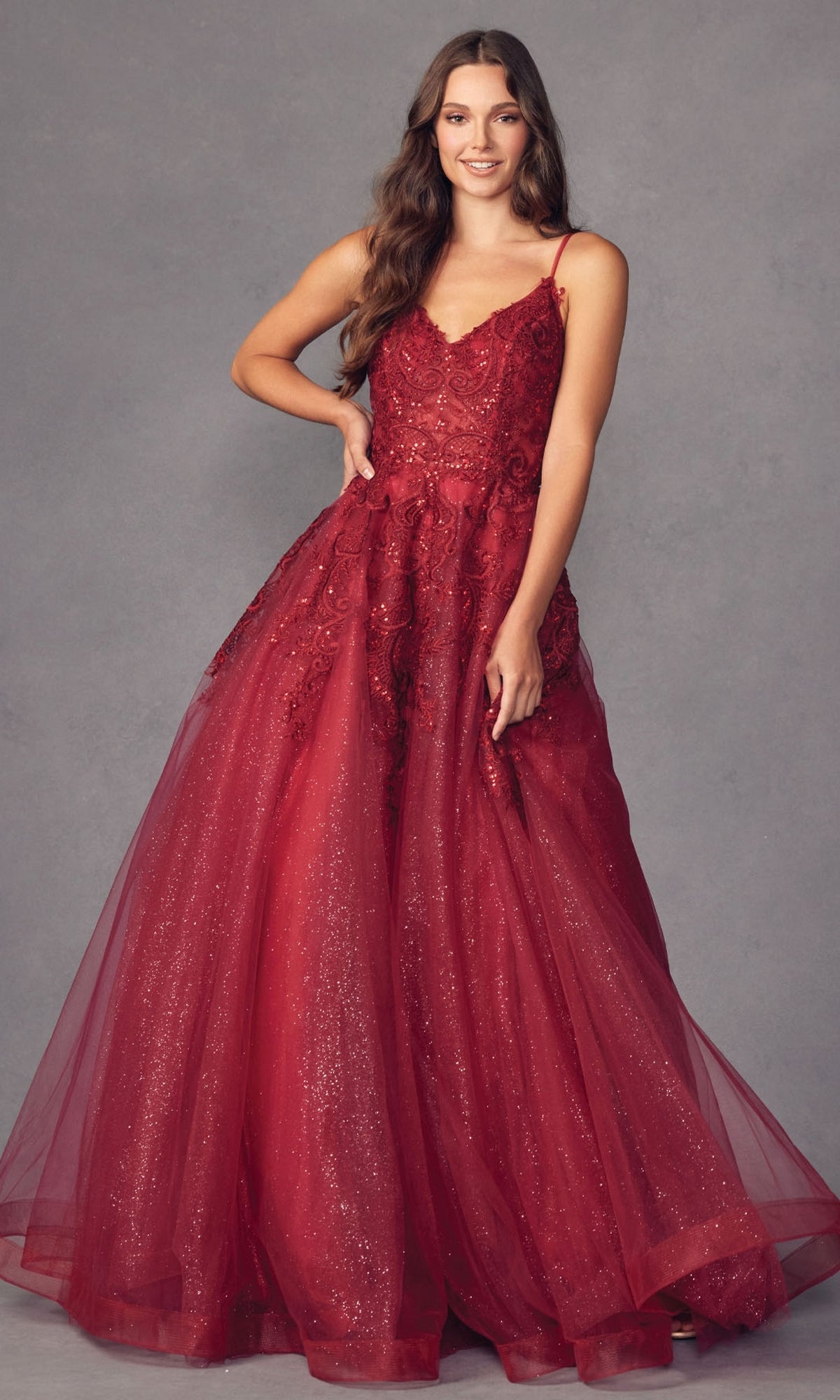 A woman models the Embroidered Glitter-Tulle Long Prom Ball Gown 251, a sleeveless, floor-length glitter dress with lace details, posing against a plain gray background.